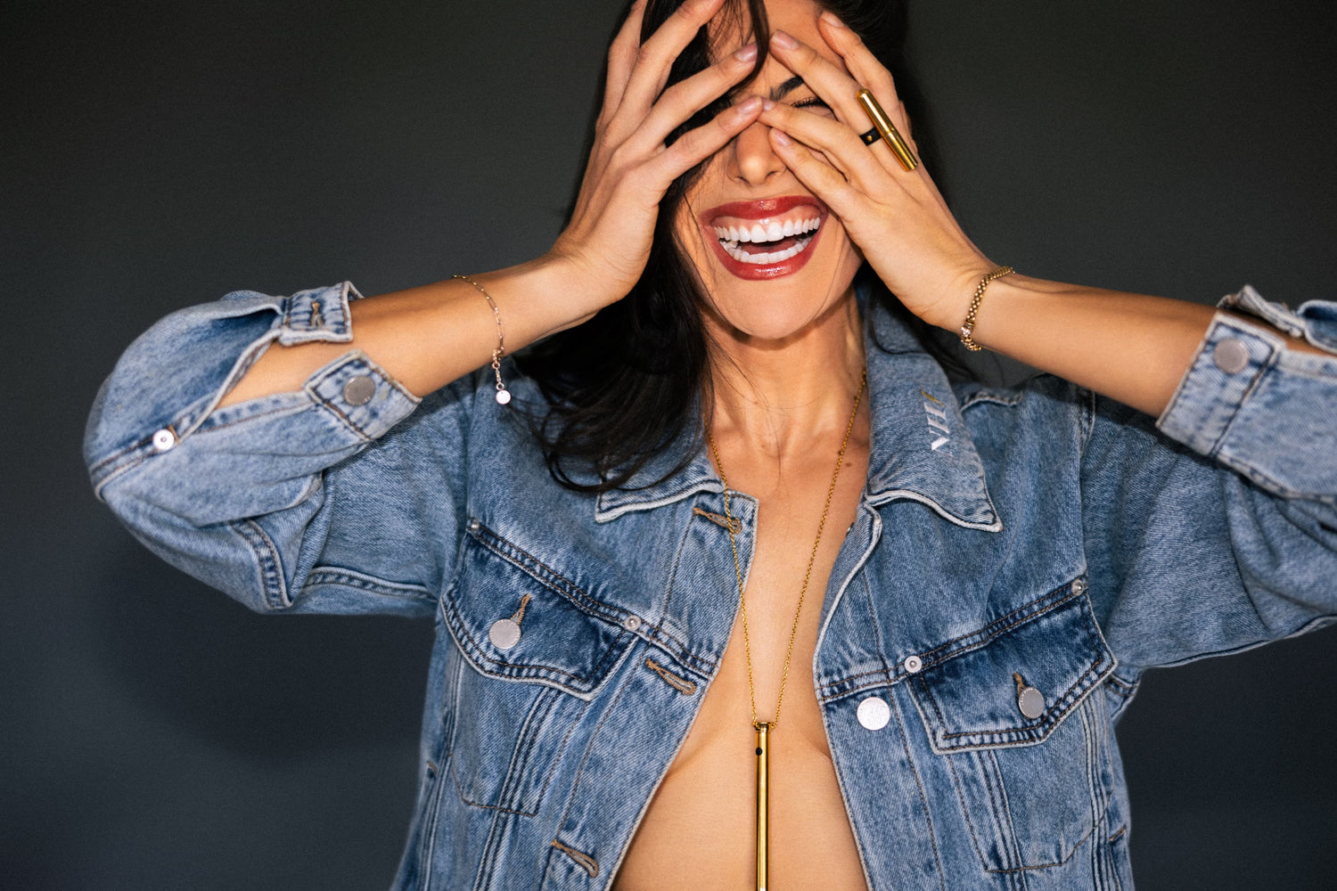 A smiling woman with hands over her eyes wearing Vesper 2 and Tease Ring in 24kt gold.