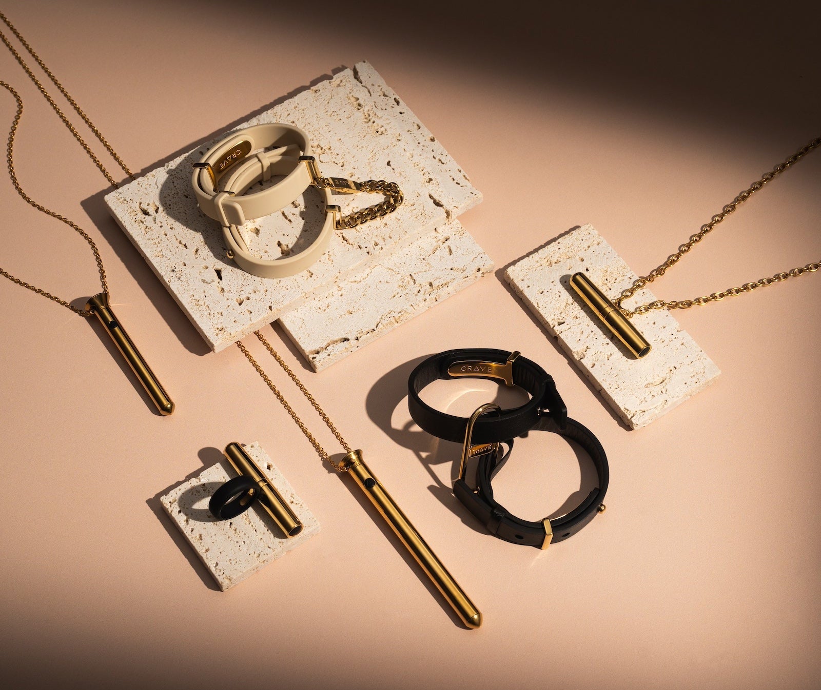 Gold and black jewelry including rings and necklaces on a beige surface with a dark background.